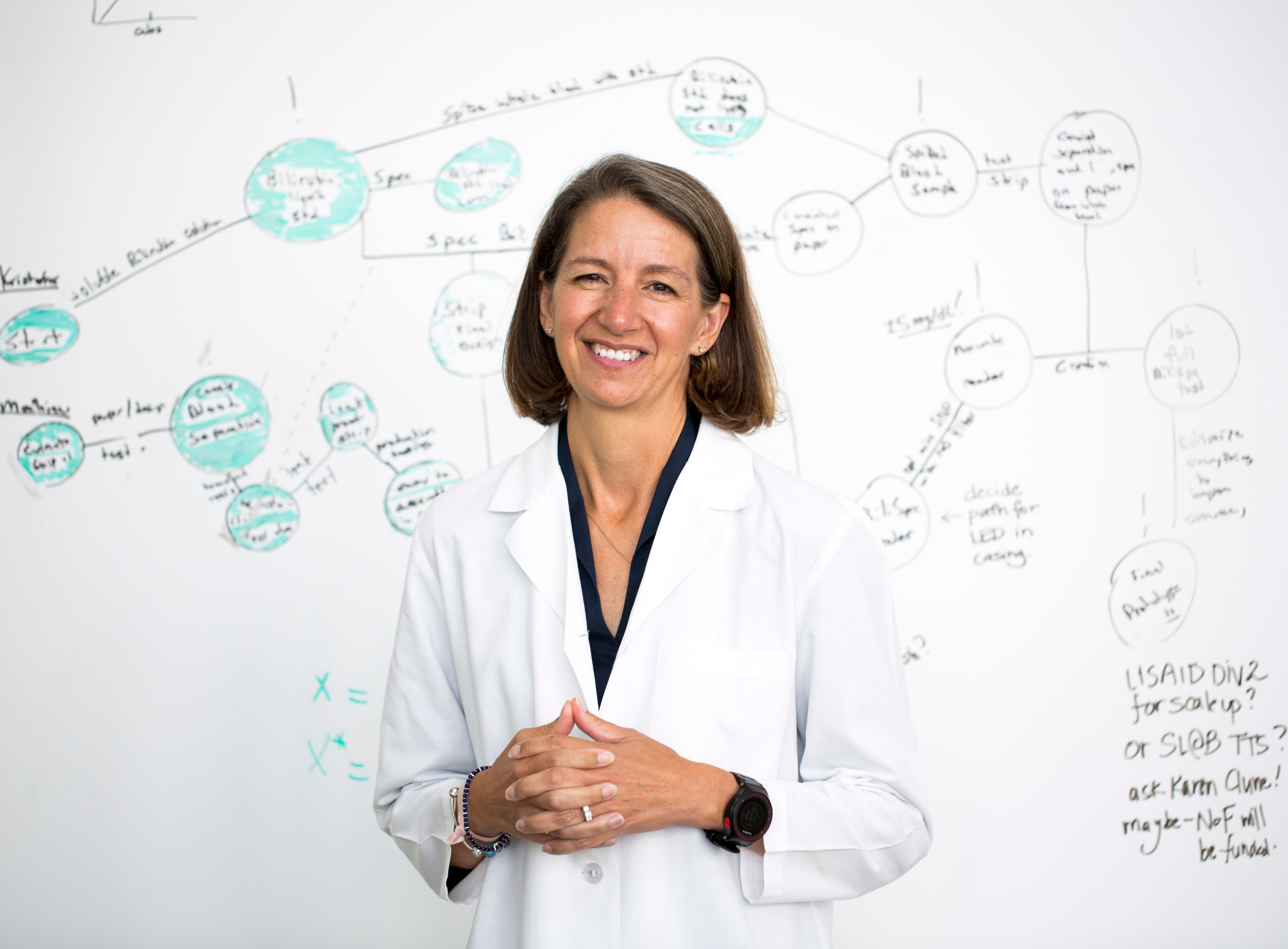 A woman with shoulder length brown hair writing on a white board in a lab.